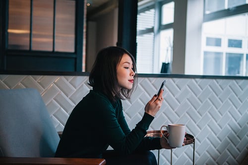 woman looking at mobile device woman looking at mobile device and holding coffee cup
