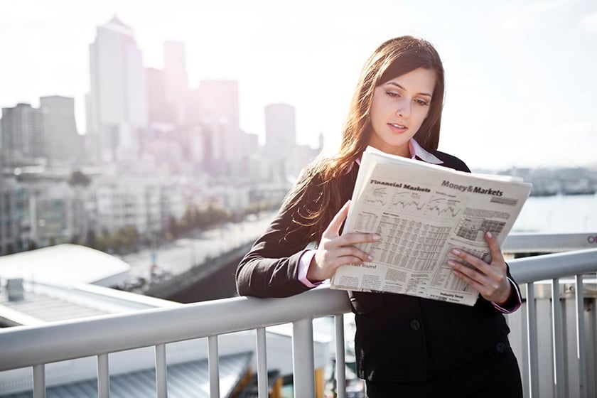 Женщина читает газету, опираясь на забор